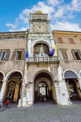 Fototapeta premium Clock tower at Piazza Grande (Great Square) in Modena showcasing historical architecture and vibrant flags during a clear blue sky