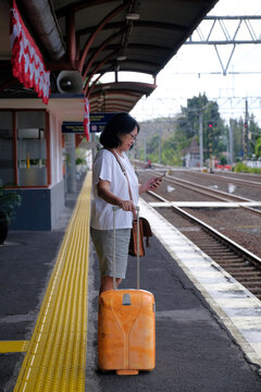 Woman holding her suitcase, standing on a railway platform, waiting for her train to arrive