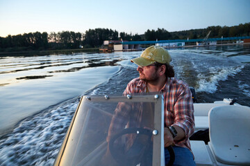 a man driving a boat on the river in the evening at sunset