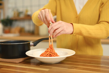 Cropped shot of young woman using chopsticks to serving pasta into a white plate