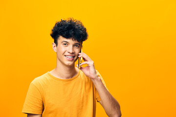 Young man smiling while talking on the phone against a bright yellow background, wearing an orange shirt, conveying joy and communication in a vibrant setting