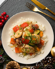 Wok-fried calmares with vegetables over white rice. Food on a table with Christmas decorations.