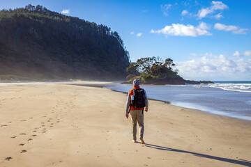 Hiker wearing a red jacket walking alone on a remote beach