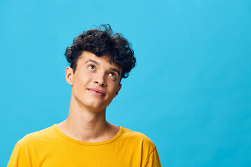 Young man with curly hair wearing a yellow shirt, looking upwards against a bright blue background, conveying curiosity and positivity Ideal for youth oriented concepts