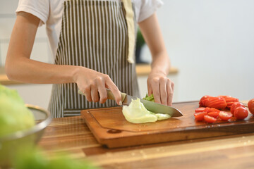 Cropped shot woman cutting lettuce on a wooden cutting board for vegetable salad