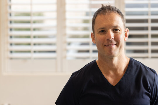 Smiling male doctor or healthcare worker in medical clinic wearing scrubs, standing confidently indo