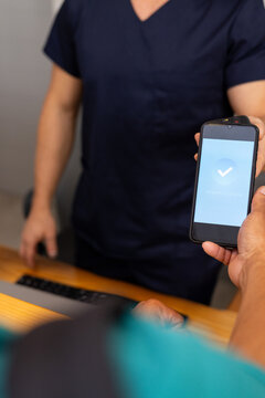 Handing smartphone with verification screen to person in scrubs at medical clinic