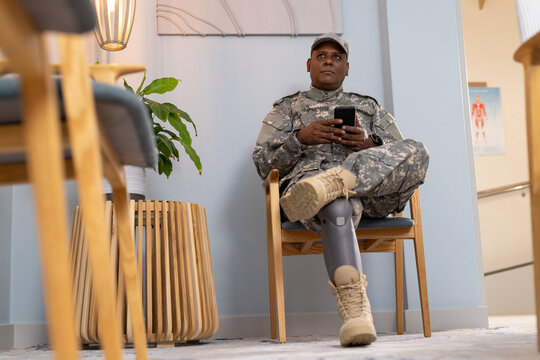 Sitting in chair, soldier with prosthetic leg using smartphone in waiting room