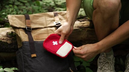 Man tourist opens travel first aid kit and takes out patch in wild forest to seal wound. Self-help in travel illustrating safety and preparedness during outdoor adventures.