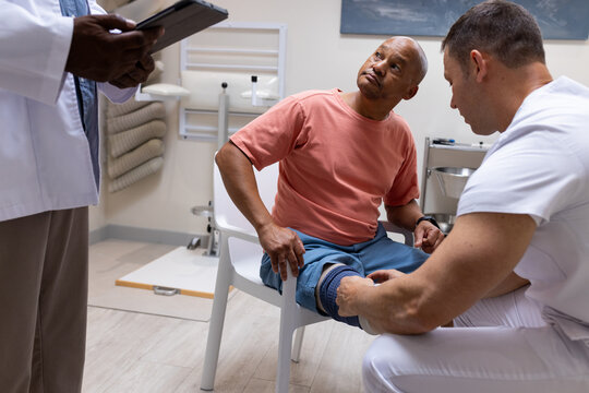 Doctor examining patient's leg while another doctor taking notes in prosthetic lab