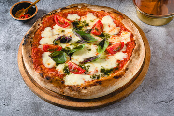 Neapolitan Margherita pizza with tomatoes, mozzarella, basil and olives on stone table