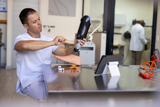 Technician in prosthetic lab adjusting artificial limb with tools on table