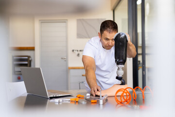 Man in prosthetic lab working on artificial limb with laptop on table