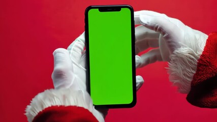 White gloves hands Santa Claus holding and showing smartphone with green chroma key screen in hands on red background, Christmas new year sale promotions, app advertisements and holiday discounts