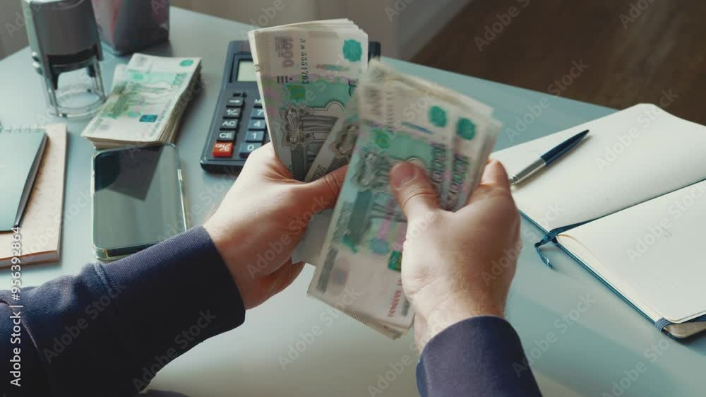 Poster counting cash at a desk with a calculator, notepad, and smartphone in a tidy office setting