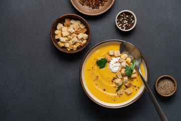Pumpkin soup with cream and bread croutons in bowl on black background. Seasonal autumn dish on the table top view