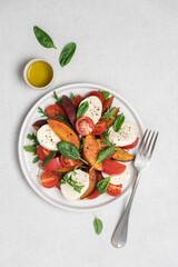 Peaches, tomatoes, mozzarella salad in plate on  white background. Caprese italian traditional salad top view