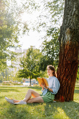 Obraz premium Young woman reading a book sitting on grass in a park