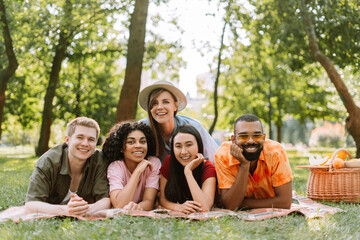 Portrait of happy multiracial friends, men and women looking at camera, relaxing, lying on blanket