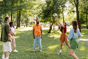 Group of young diverse, multinational people playing football in park, free time, picnic concept