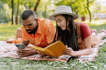 Young couple enjoying summer relaxing in park reading and browsing smartphone