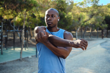 African athletic man dressed in sleeveless blue shirt, black shorts do shoulder stretching warming...