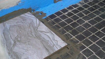 Installation of floor tiles. The tiles are glued to the floor with adhesive applied with a notched trowel. Laying ceramic tiles on the floor. 