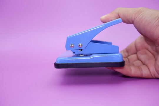 hand holding a blue paper hole punch. paper hole punch isolated on purple background. - Powered by Adobe