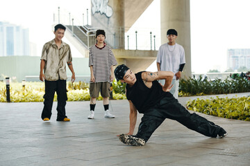 Breakdancer showing impressive move on urban pavement with three onlookers standing in background...