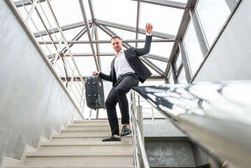 Happy businessman wearing formal suit sliding on stairs Railing in modern business building. Hurry...