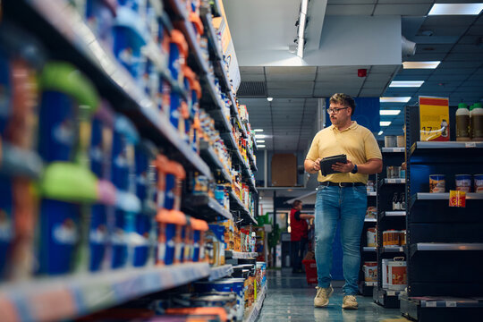 Employee examining products in a retail store aisle while taking notes during the day