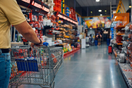 Man pushing a shopping cart through a retail store aisle filled with tools and supplies during daytime hours