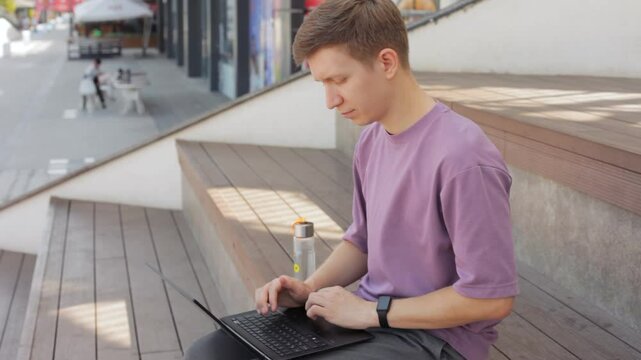Young man sitting on bench and working on laptop. 