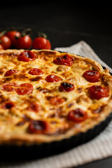 Pie Quiche Lorraine with tomatoes and melted cheese on the table close-up. Copy space.