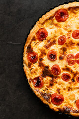 Pie Quiche Lorraine with tomatoes and melted cheese on the table close-up. Copy space.