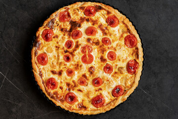 Pie Quiche Lorraine with tomatoes and melted cheese on the table close-up. Copy space.