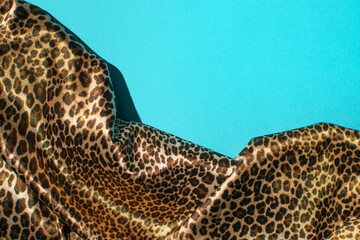 Creative composition, turquoise blue background and leopard print satin fabric.
