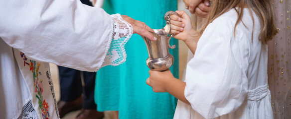 Little girl holding a jug with holy water during baptism ceremony.