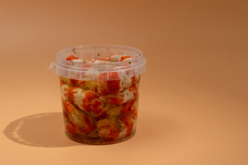 On the table is a container with Surimi in the form of shrimp. The shrimp are in oil and arranged so that they look appetizing. Surimi on an orange background.