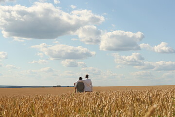 Young adult son and father together in the wheat field on a light blue sky background. Photo was taken 26 July 2024 year.