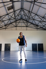 Holding basketball, athlete standing on indoor court, preparing for practice, copy space