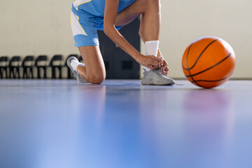 Naklejka premium Tying shoelaces, female basketball player preparing for game on court, copy space