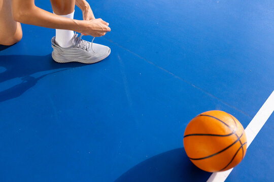 Tying shoelaces on basketball court, woman preparing for game with ball nearby, copy space