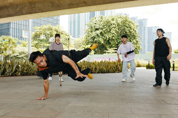 Group of breakdancers showcasing energetic skills on urban pavement, surrounded by green foliage...
