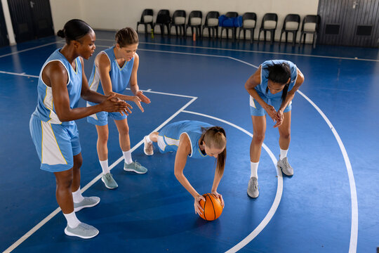 Female basketball players training, one doing push-ups with ball on court
