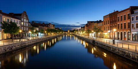 Obraz premium An enchanting view of a city canal at dusk with streetlights reflecting in the calm water, lined with historic buildings, creating a tranquil and romantic atmosphere.