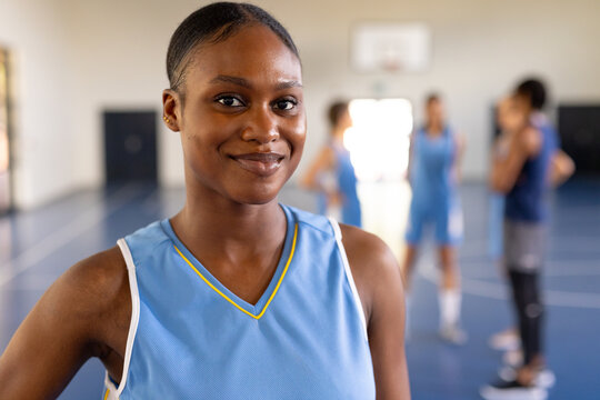 Smiling female basketball player in uniform standing on court with teammates