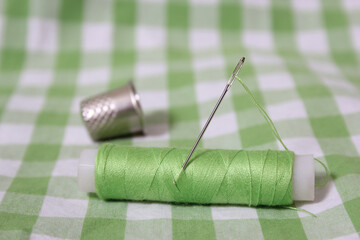 Spool of Green Thread, Thimble and Needle on Green Checkered Fabric