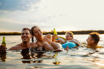 Group of young friends having fun and enjoying a summer day swimming with rubber tube and drinking...