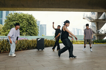 Fototapeta premium Four young men breakdancing in urban landscape surrounded by graffiti-covered walls performing dynamic dance moves. City skyscrapers visible in background creating contrast with street setting